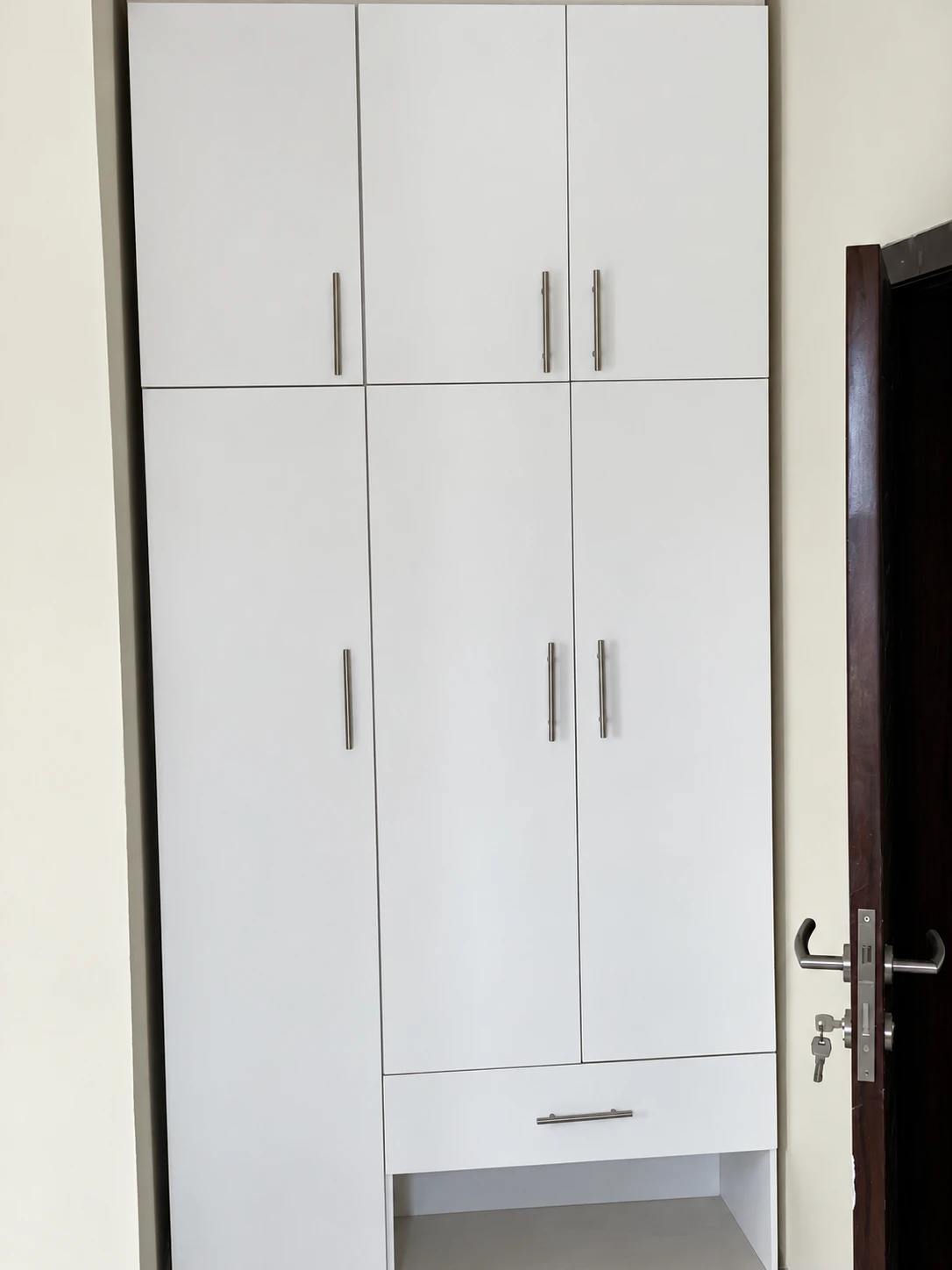 Floor-to-ceiling wardrobe fitted into an alcove beside the door, with a drawer and open shelf